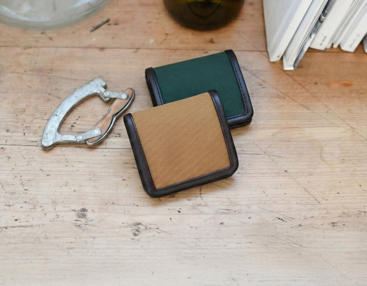 Square wallets  on a wooden surface with books and a bottle in the background